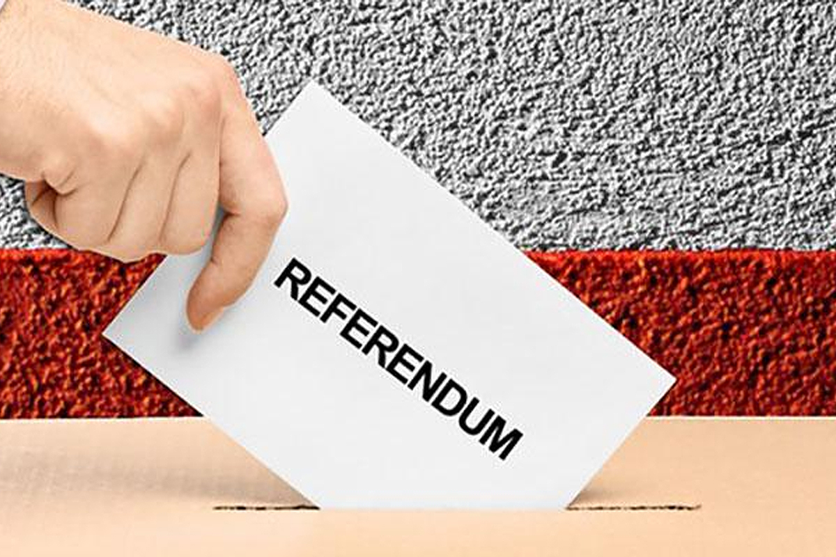 Mano che imbuca  in urna foglio bianco con scritta in maiuscolo nero "REFERENDUM"